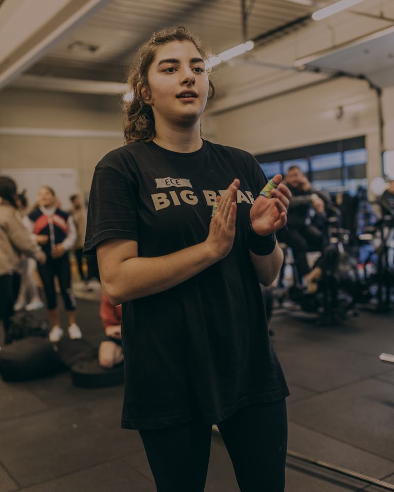 Athletin im BIG BEAR Shirt klatscht in die Hände, dahinter die Gruppe beim Training